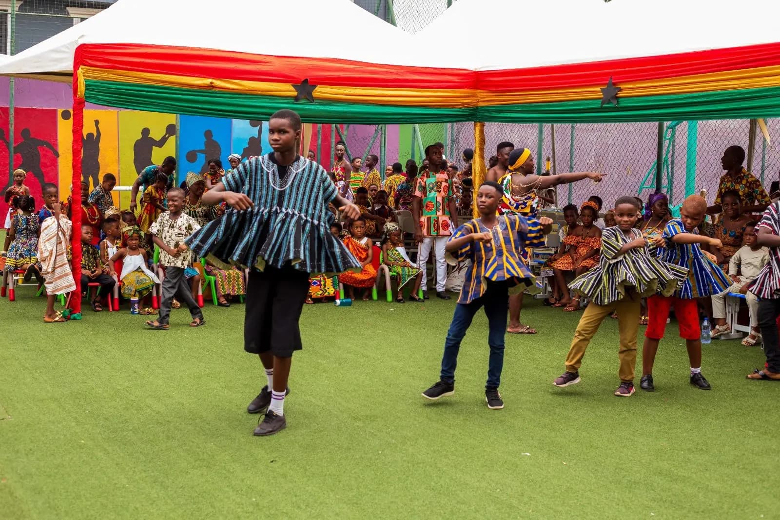 HABIS pupils in striped smocks performing in front of a red yellow and green canopy
