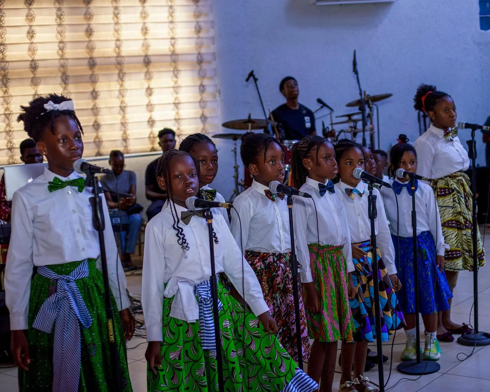 HABIS pupils in white shirts and patterned wraps lined up at microphones
