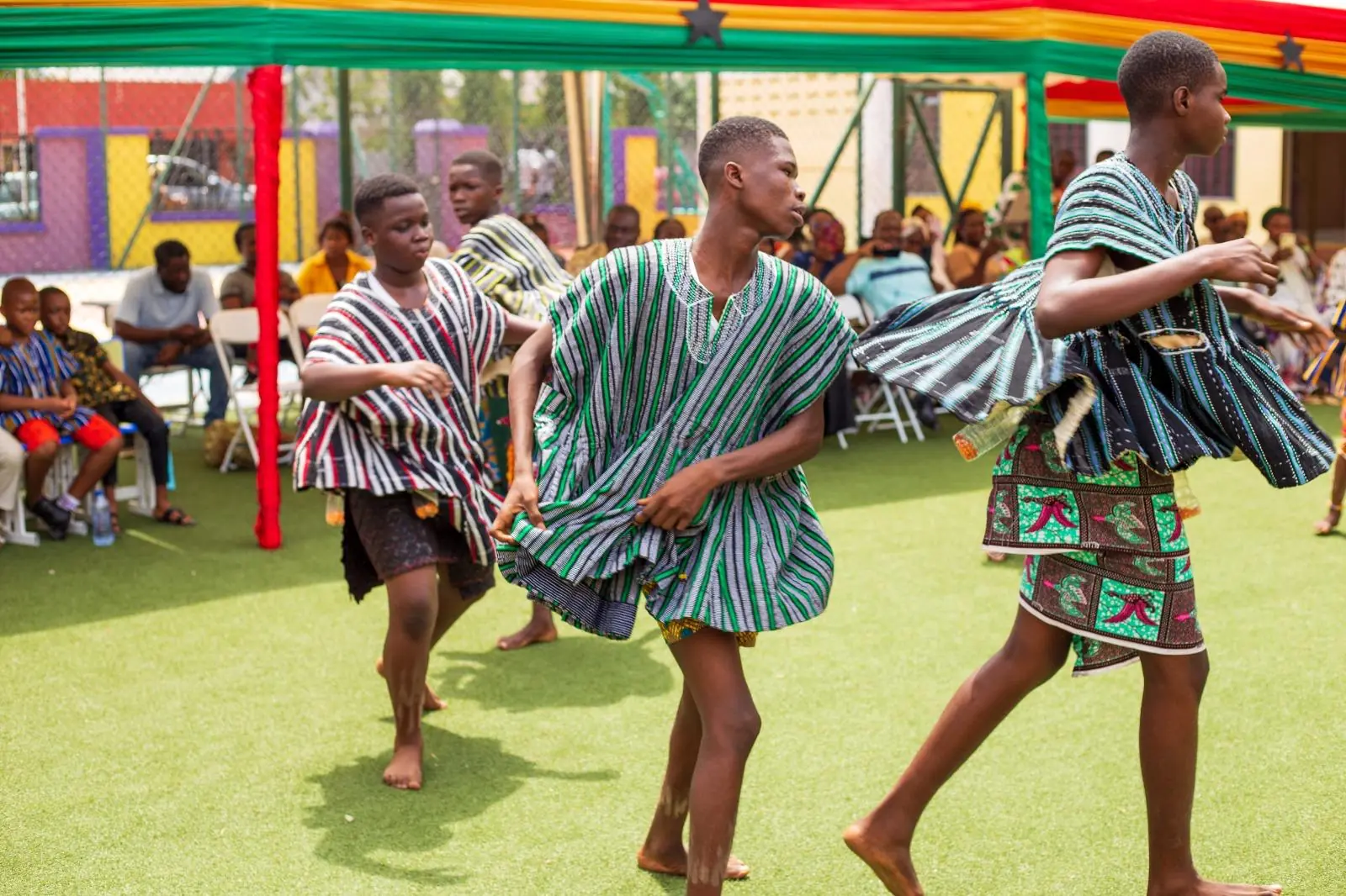 Three HABIS pupils in striped smocks dancing together outdoors