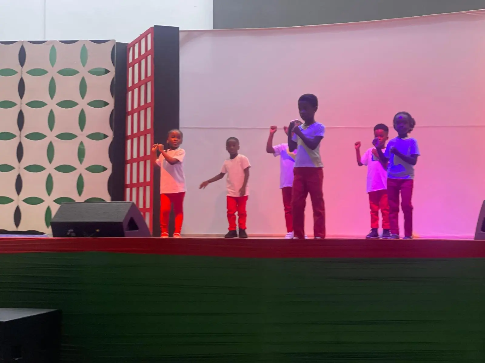 Young performers speaking into microphones on a stage lit in pink and purple