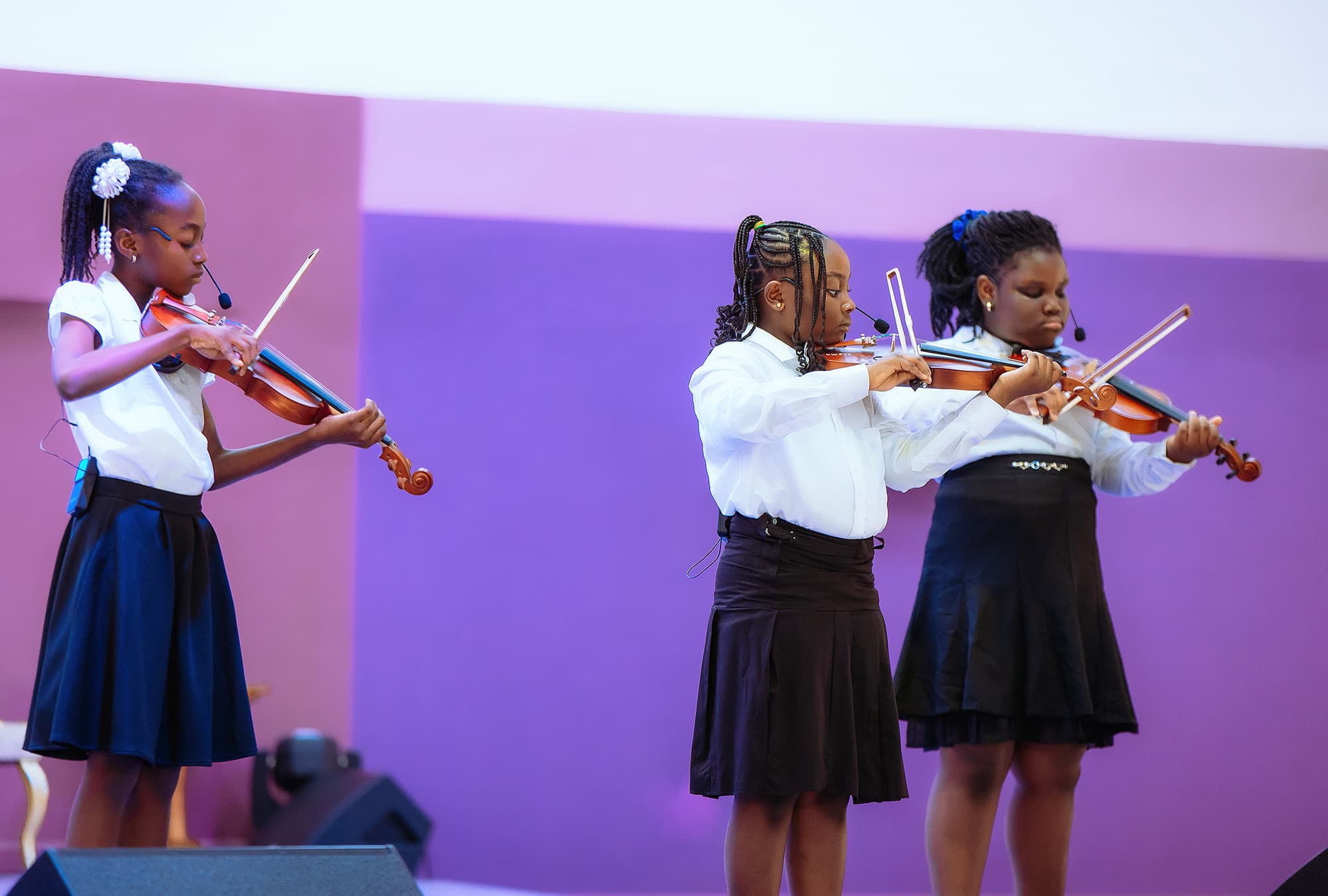 Three HABIS students playing violins together on stage