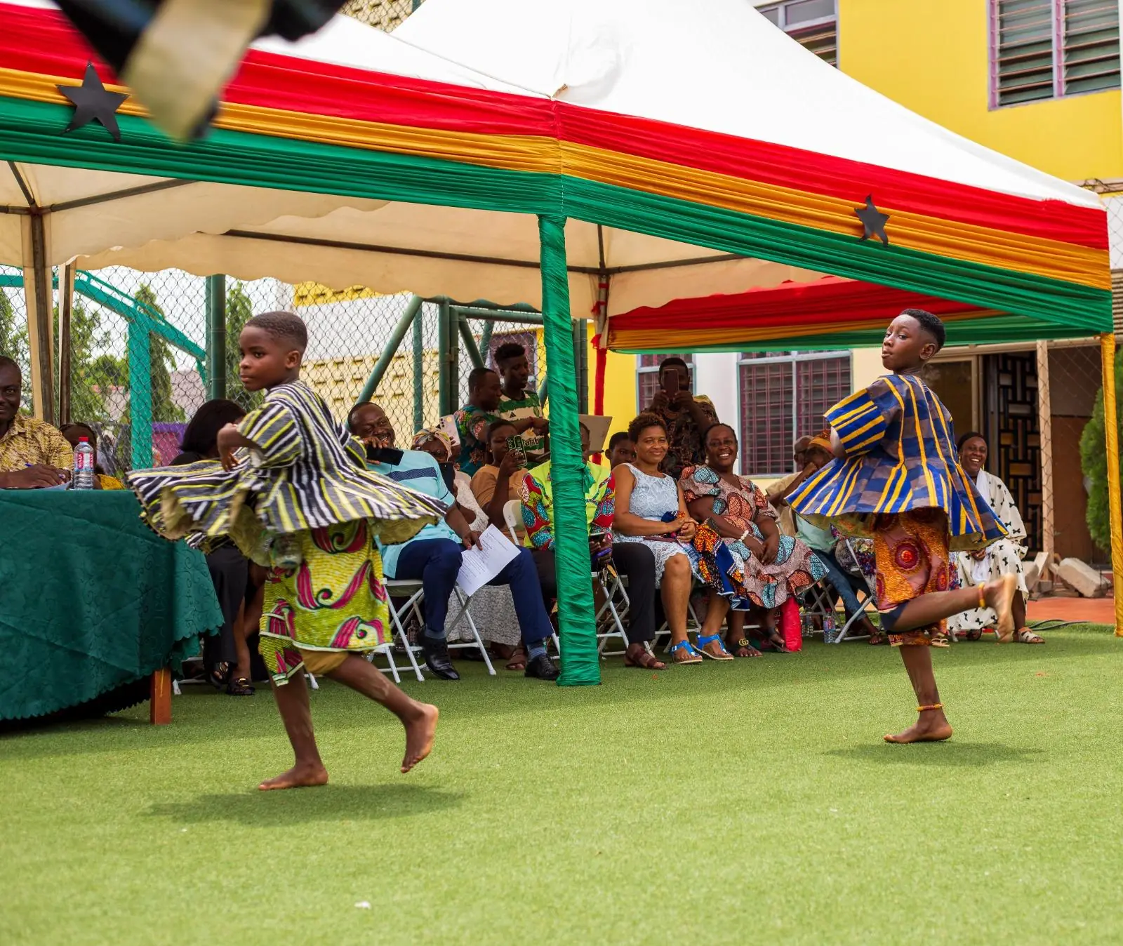 Two pupils in striped traditional smocks dancing beside a decorated canopy